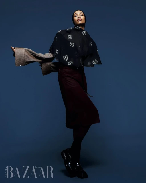 A stylish portrait features a woman in a black floral top and maroon skirt against a blue backdrop, showcasing a high-fashion pose and attire.
