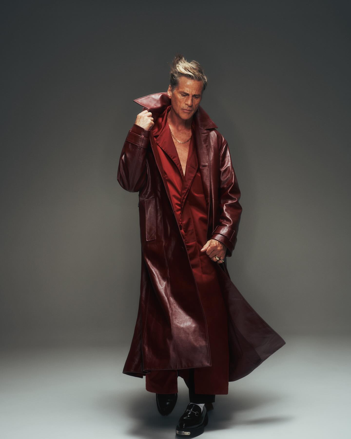 Portrait of a male fashion model wearing a maroon leather coat and pants in a studio setting with a neutral background.