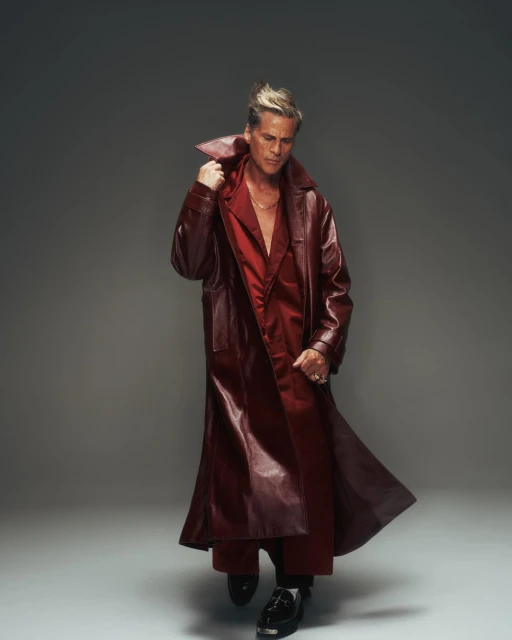 Portrait of a male fashion model wearing a maroon leather coat and pants in a studio setting with a neutral background.