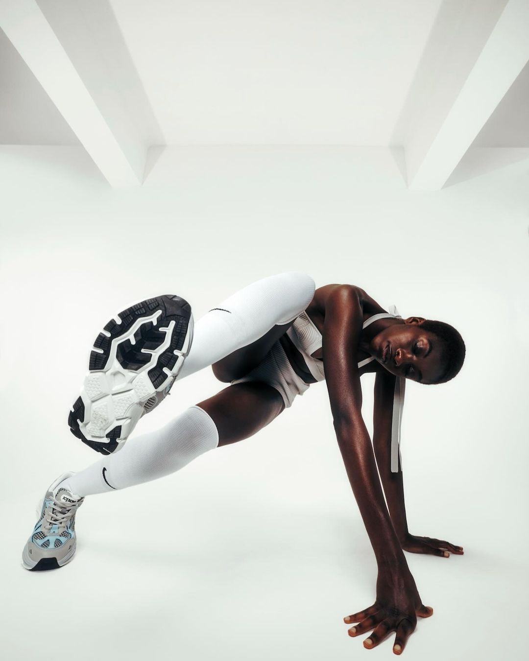 Athletic woman in white sportswear and sneakers performs gymnastic pose on white backdrop in studio. Fitness and sport concept.
