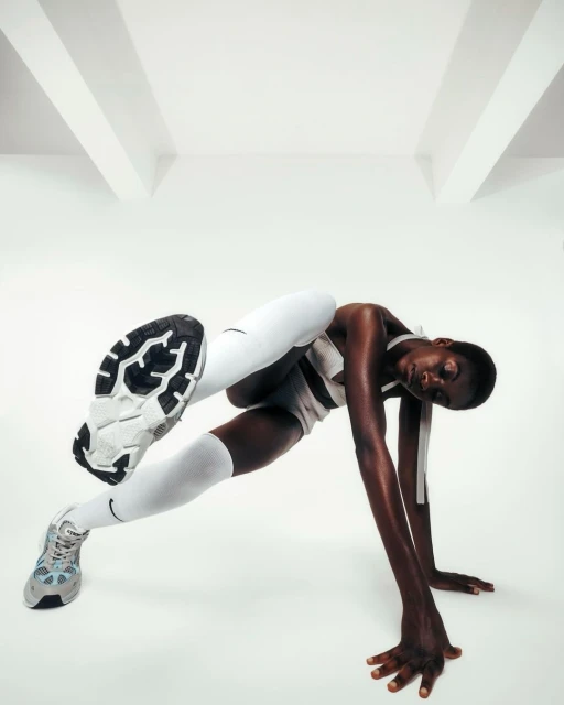Athletic woman in white sportswear and sneakers performs gymnastic pose on white backdrop in studio. Fitness and sport concept.