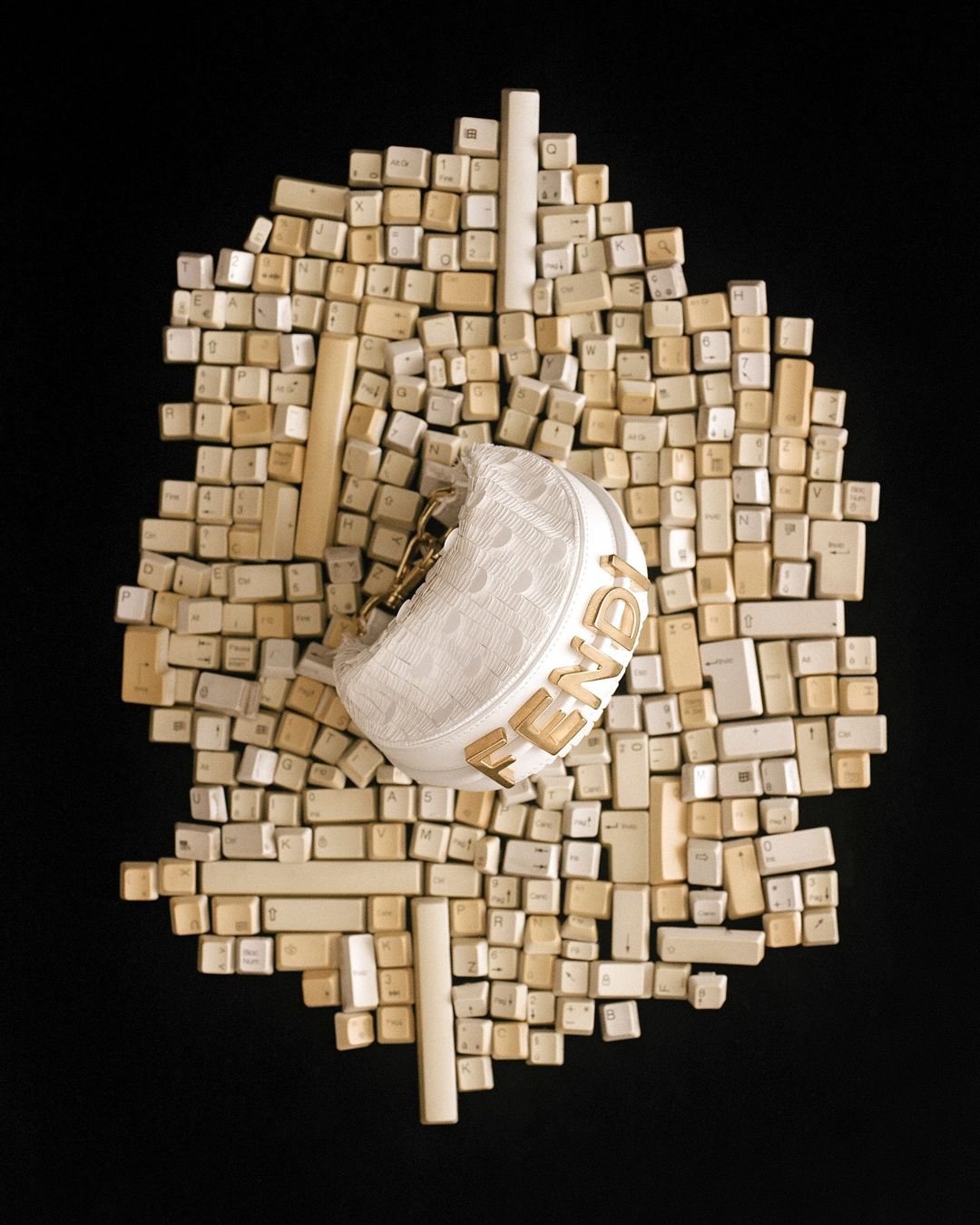 High-angle shot of a designer purse, white with a Fendi logo, placed on a collection of computer keys against a black background.