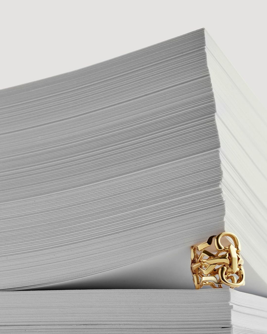 Close-up shot of a gold chain link ring sitting on a stack of white paper, macro shot of a piece of jewelry.