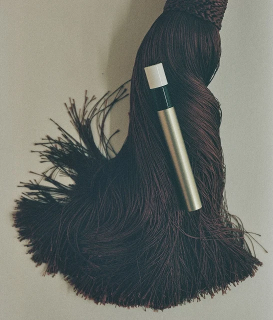 Close-up studio shot: brown tassel with a sleek gold and white perfume tube, creating a minimalistic beauty product presentation.