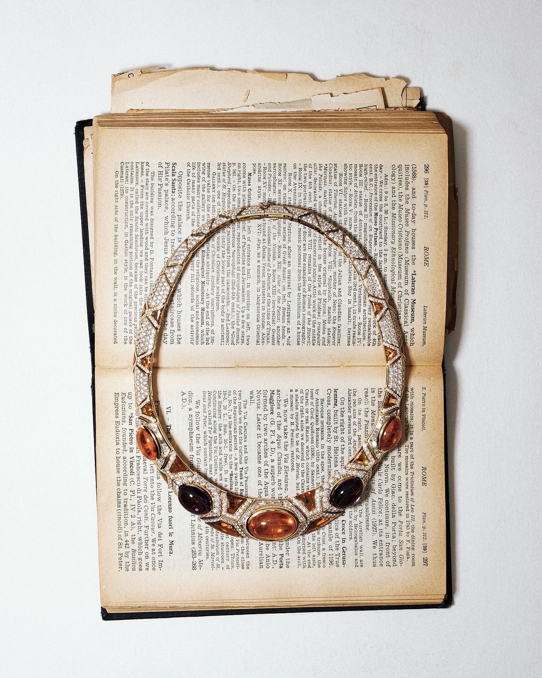 Elegant gold necklace with amber and black gemstones on open antique book with textured pages, illuminated by soft lighting.