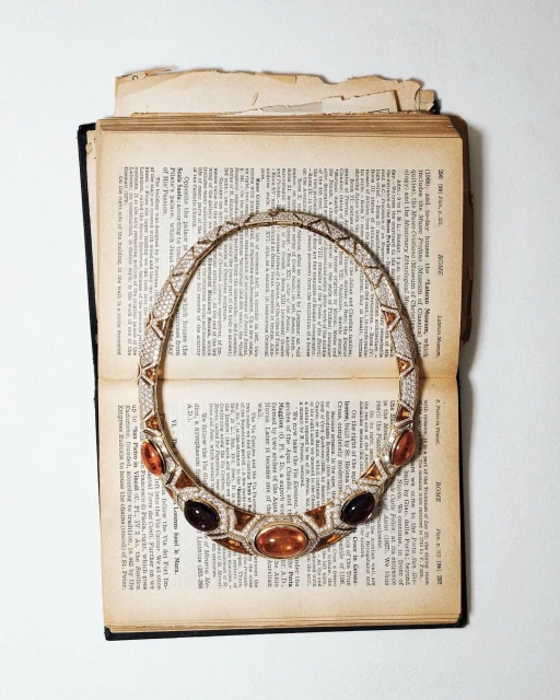 Elegant gold necklace with amber and black gemstones on open antique book with textured pages, illuminated by soft lighting.