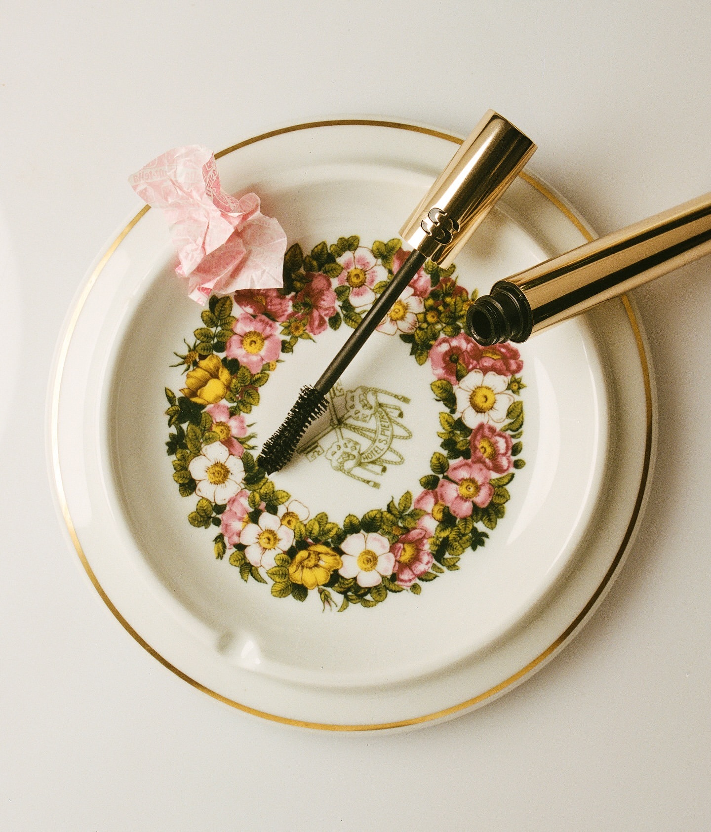 Mascara wand and tube on a floral-patterned plate. Makeup product in a close-up studio shot for beauty and cosmetics advertising.
