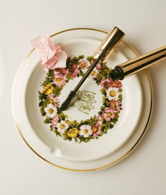 Mascara wand and tube on a floral-patterned plate. Makeup product in a close-up studio shot for beauty and cosmetics advertising.