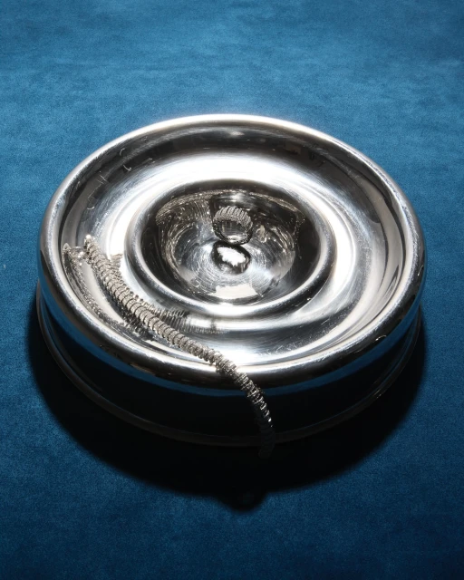 Silver candle holder with a metal coil on a blue velvet surface, highlighting texture and light in a simple, elegant composition.