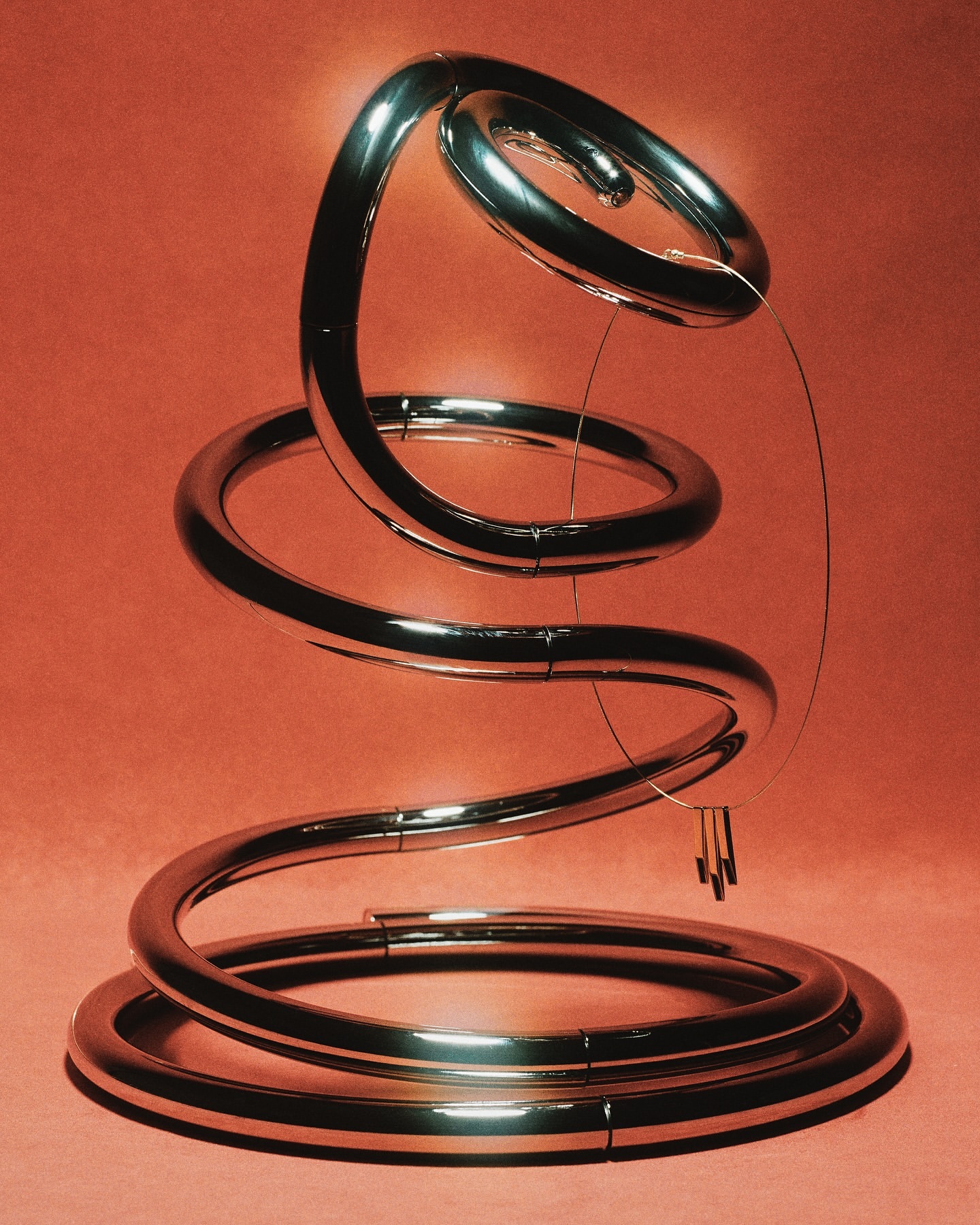 Abstract sculpture of a polished, chrome-like metal coil or spiral with a small set of chimes hanging from thin wires.
