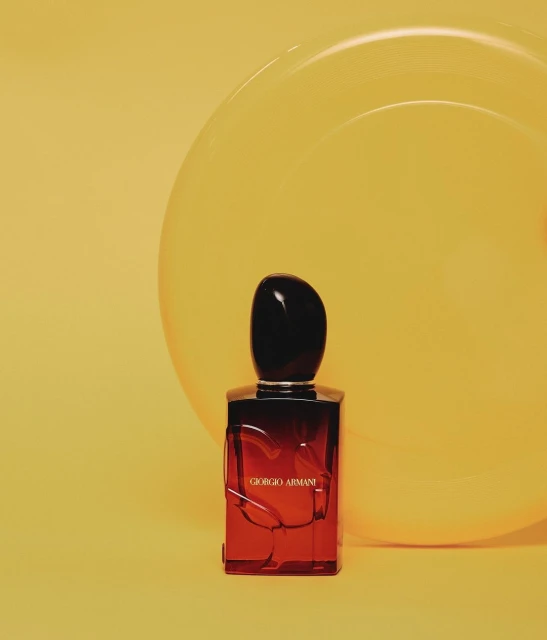 Giorgio Armani perfume bottle with a black cap on a red container with a glossy yellow sphere in the background.