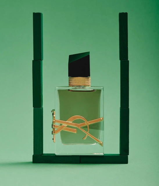 Elevated, studio shot of Yves Saint Laurent cologne bottle against green backdrop, framed by dark green wooden blocks, evoking luxury.