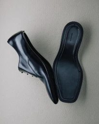 Top-down view of two black leather dress shoes displayed against a textured off-white background by photographer Mattia Iotti.