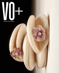 Two intricate flower-shaped diamond and gemstone rings resting on sculpted cream-colored organic forms against a stark black and white background
