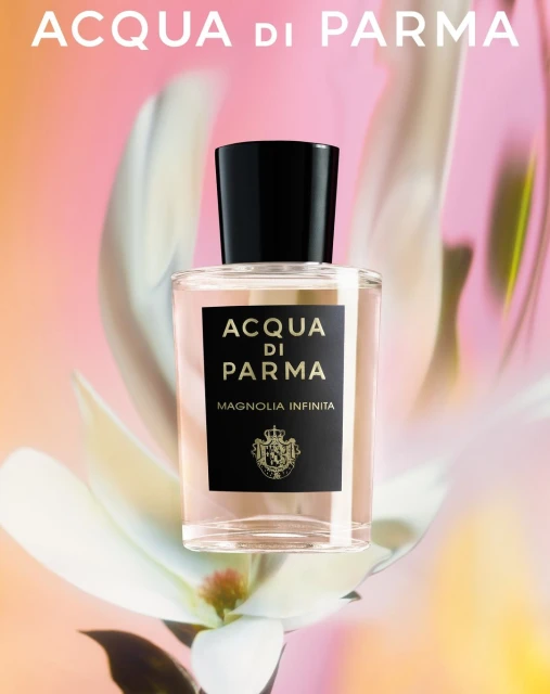 A perfume bottle from ACQUA DI PARMA, MAGNOLIA INFINITA on a background with blurred flower petals and soft gradient pink tones.