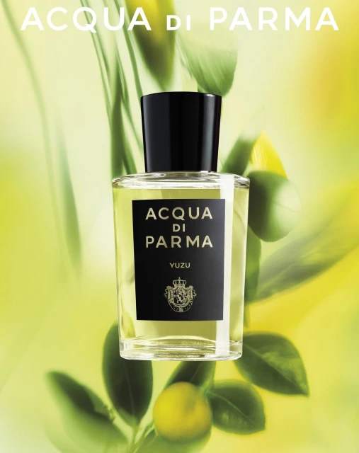 Acqua di Parma Yuzu fragrance bottle against a blurred green backdrop with leaves and fruit, product shot, beauty and personal care.