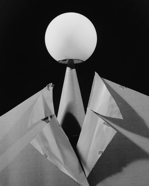 Monochrome still life with spherical lamp above paper jacket in a dark studio setting, creating an intriguing abstract composition.