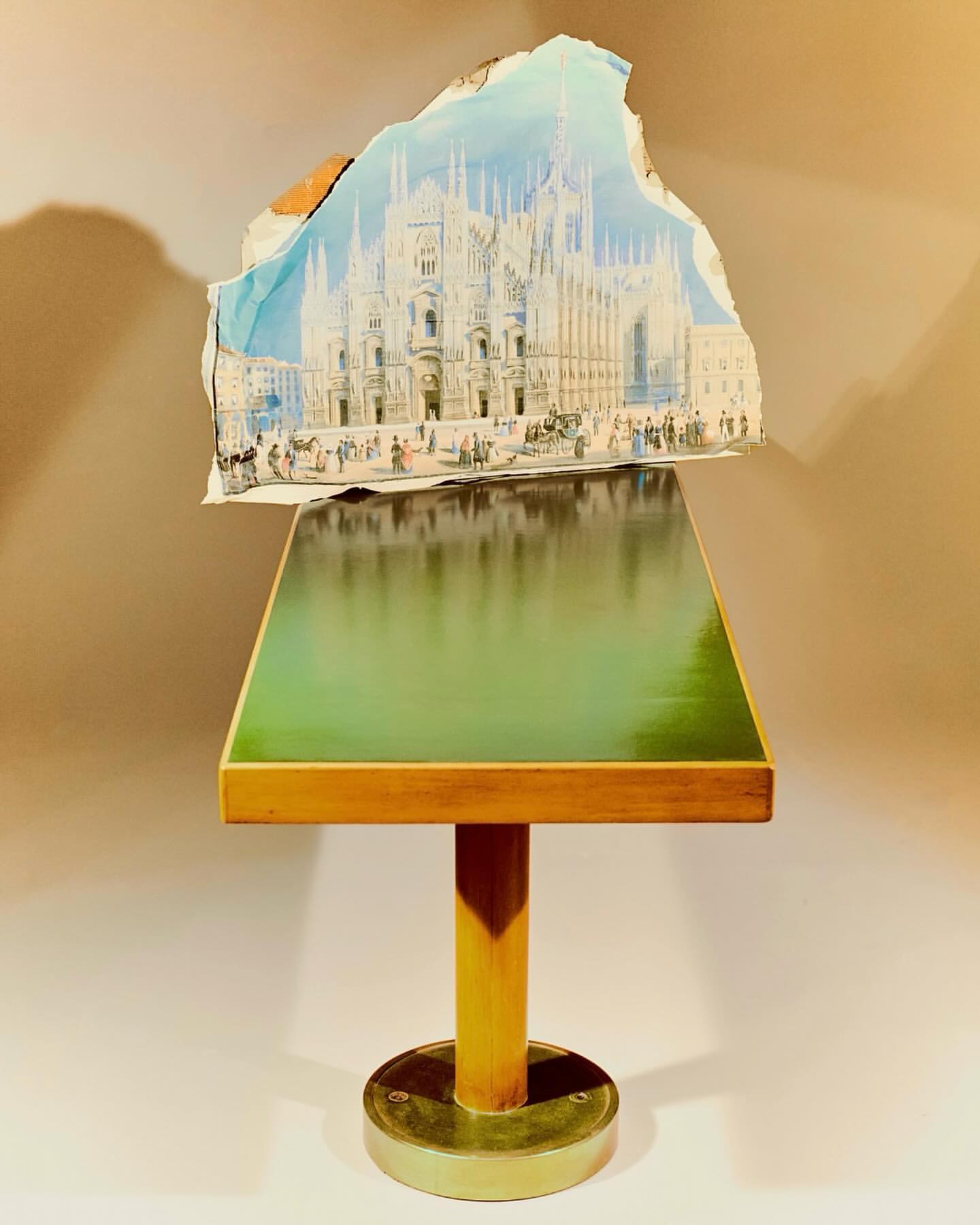 Unique still life of a table with a green top supporting a torn poster of a historic building, evoking a vintage and artistic mood.