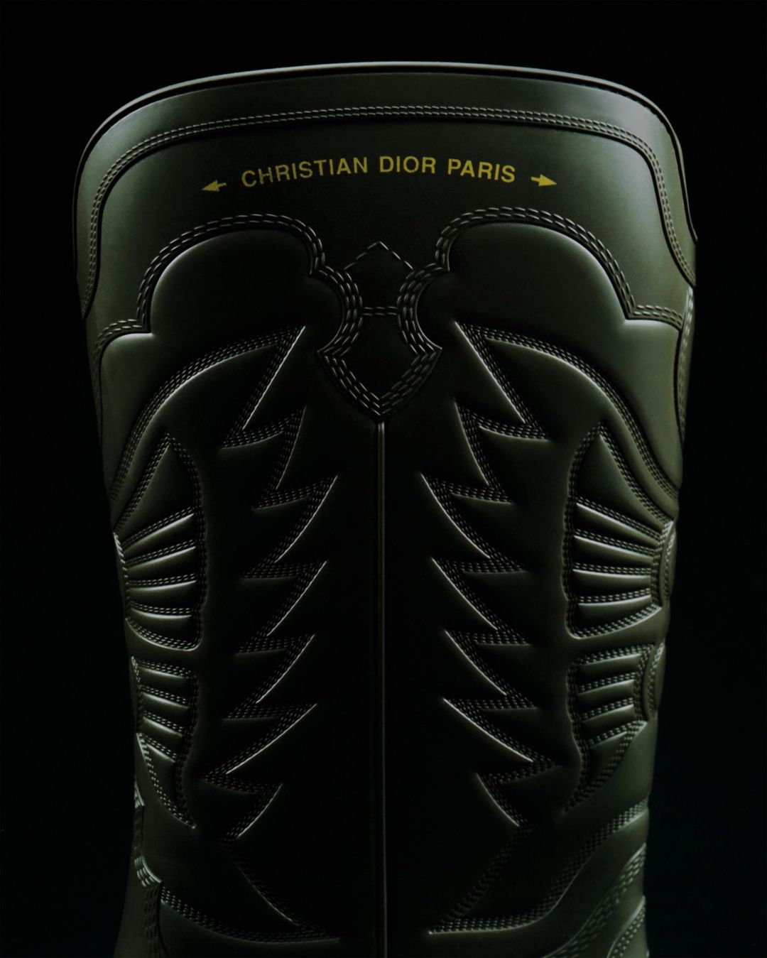 Close-up of a black Christian Dior Paris boot with detailed stitching, set against a dark background.