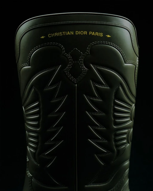 Close-up of a black Christian Dior Paris boot with detailed stitching, set against a dark background.
