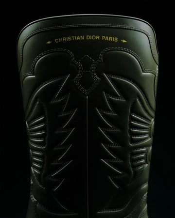 Close-up of a black Christian Dior Paris boot with detailed stitching, set against a dark background.