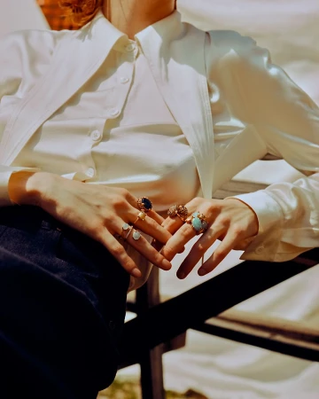 Close up of woman wearing multiple gemstone rings on her fingers and a white button up shirt by Mattia Parodi