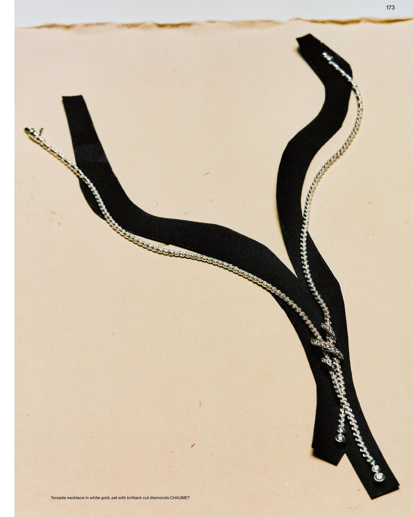 Abstract display of a black strap necklace with silver chain detailing on a beige surface, showcasing modern jewelry design.