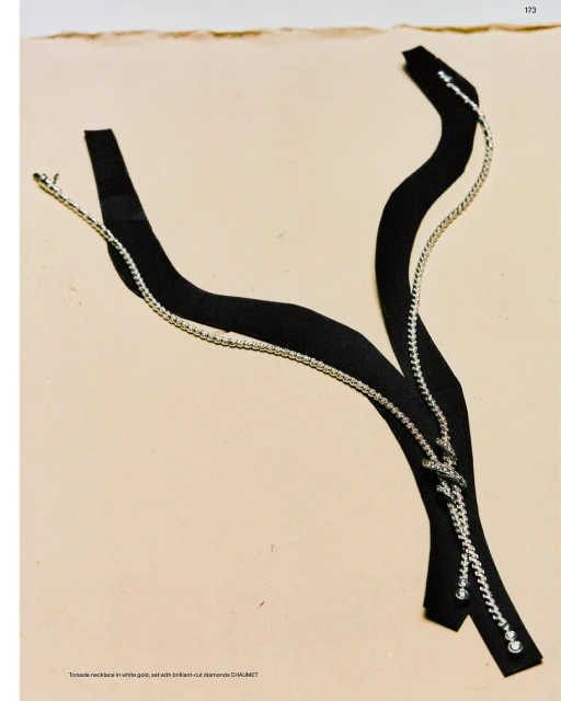 Abstract display of a black strap necklace with silver chain detailing on a beige surface, showcasing modern jewelry design.