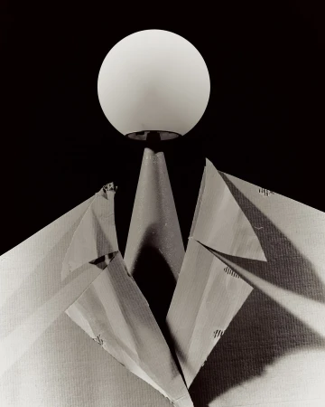Abstract still life of an illuminated sphere atop a conical stand, with a paper jacket forming lapels, against a dark background.