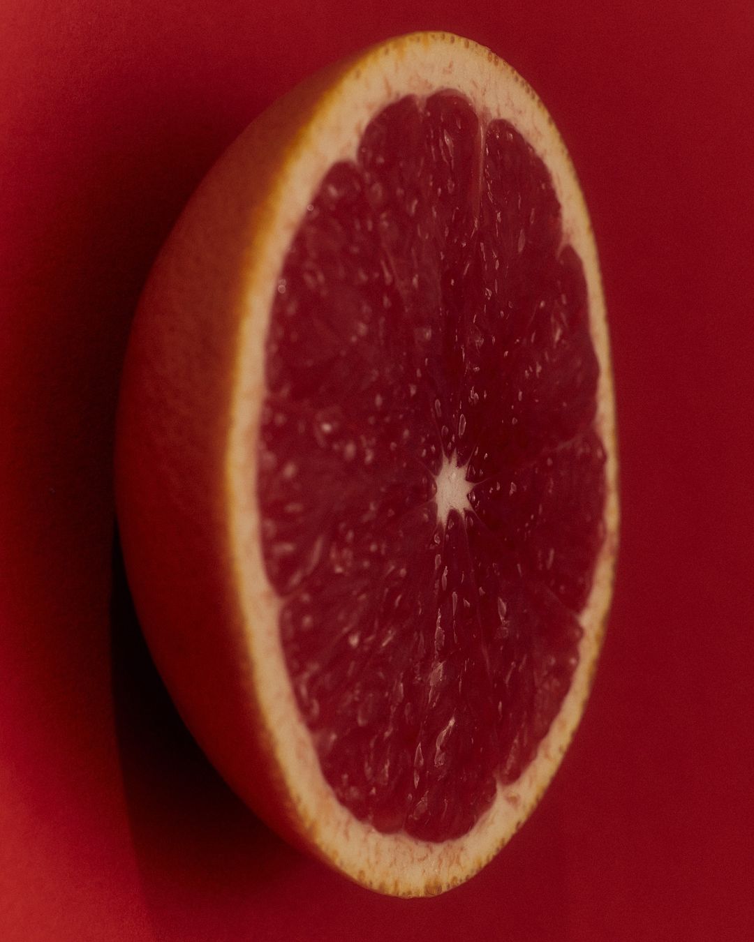 Close-up photograph of half of a red grapefruit with a red background, showcasing the fruit's texture and color.