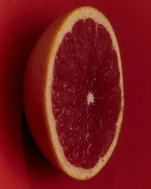 Close-up photograph of half of a red grapefruit with a red background, showcasing the fruit's texture and color.