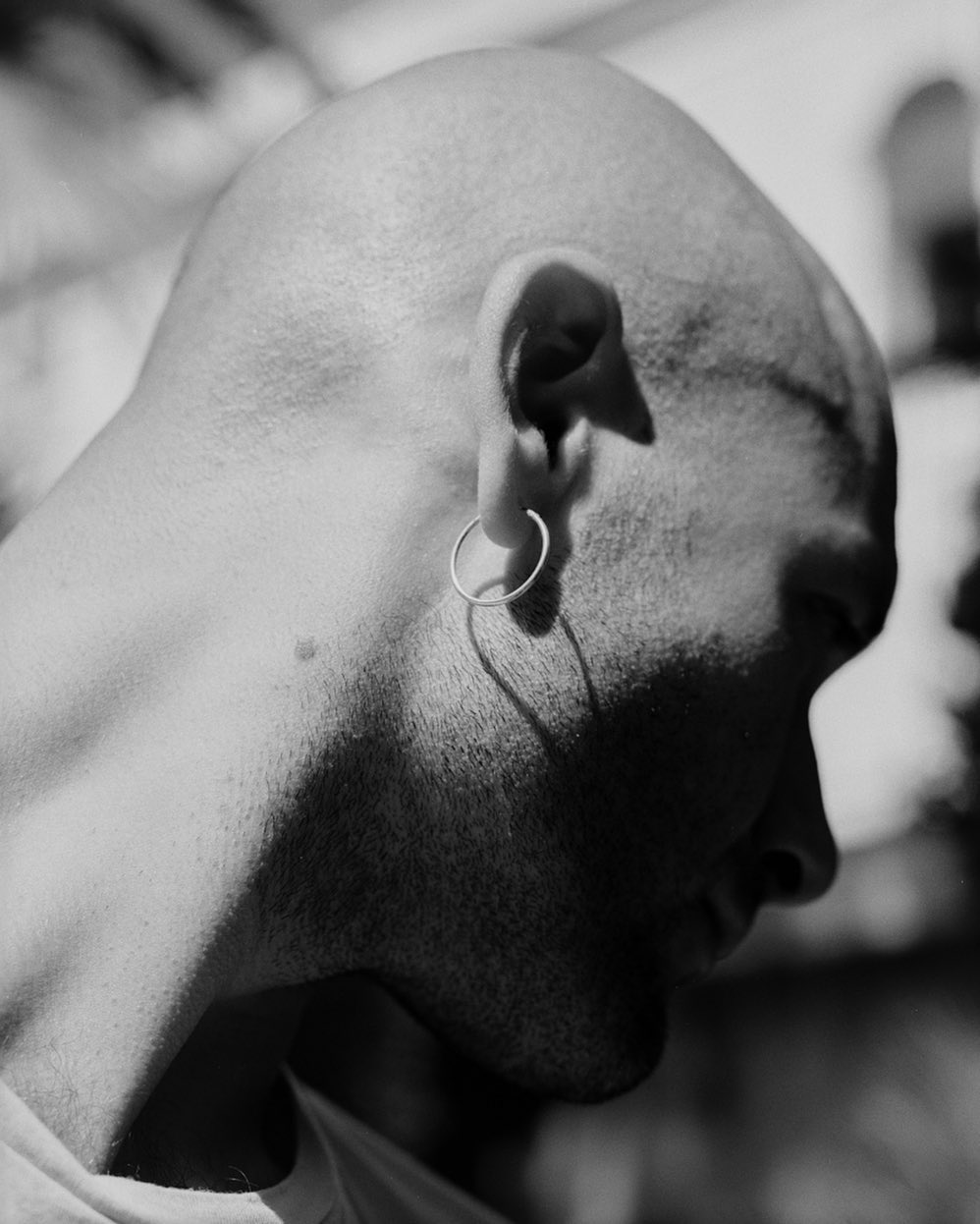 Close-up black and white studio shot of a bald adult male wearing a hoop earring, focusing on the side of his head and ear.