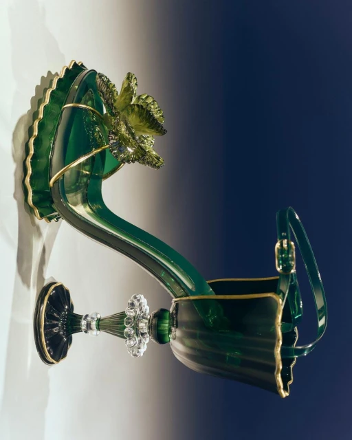 Elegant green glass decorative shoe with gold trim and floral detail. Artistic footwear design with a mix of glossy and transparent elements.