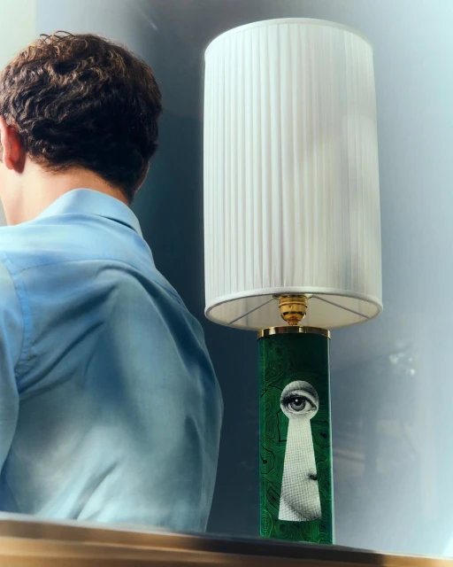 Lamp with a keyhole design and an eye, situated next to a person wearing a blue shirt. The scene is brightly lit indoors.
