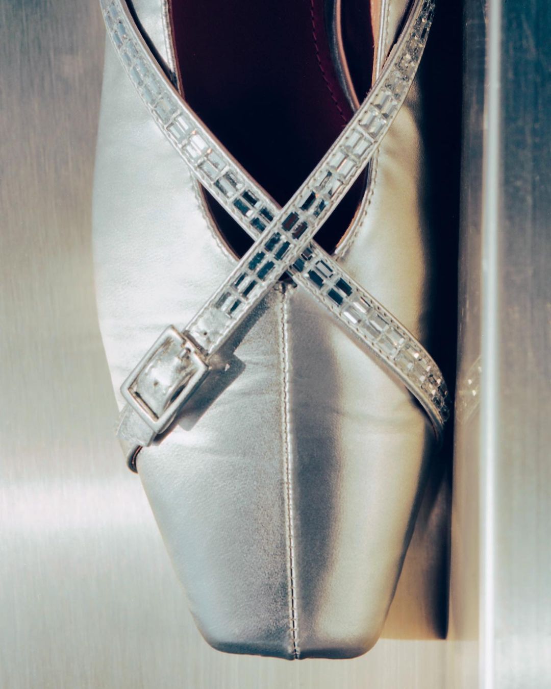 Elegant silver ballet flat shoe with jeweled straps and buckle detail, set against a clean, minimalist background. Close-up product photography.