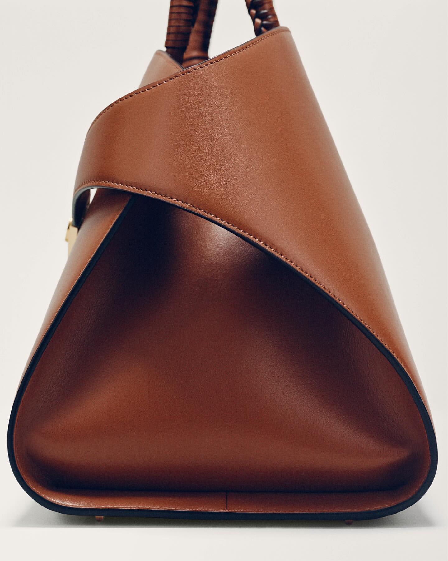 Studio shot of a brown leather handbag featuring braided handles, showcasing its geometric design and craftsmanship against a white backdrop.