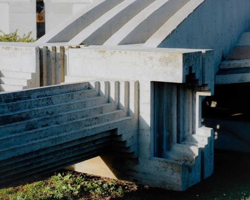 Close-up of a Brutalist-style concrete structure with stairs and geometric forms, set outdoors with some greenery visible.