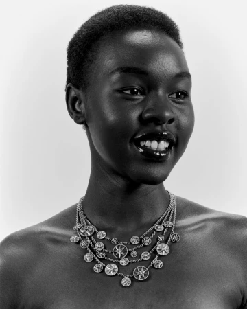 Portrait of a smiling Black woman wearing a multi-strand silver pendant necklace against a light background