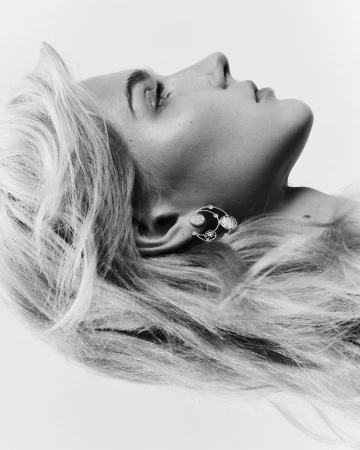 Close-up profile portrait of a blonde woman wearing an intricate silver earring against a plain white background.