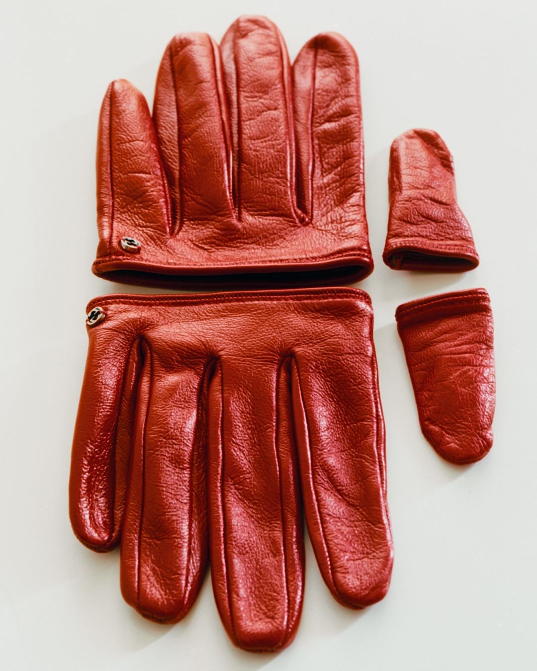 Two pairs of red leather gloves with fingerless tips are laid out on a white surface, showcasing their unique design and craftsmanship.