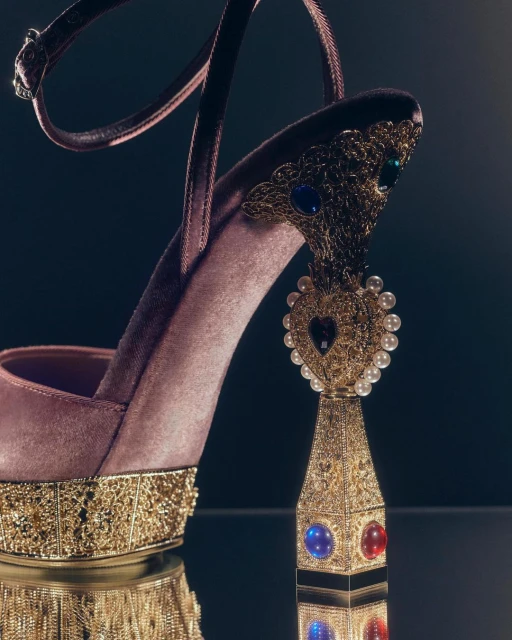 Close-up of an elegant platform high-heel shoe with an ankle strap, featuring a gold-tone decorative heel and a reflective surface.