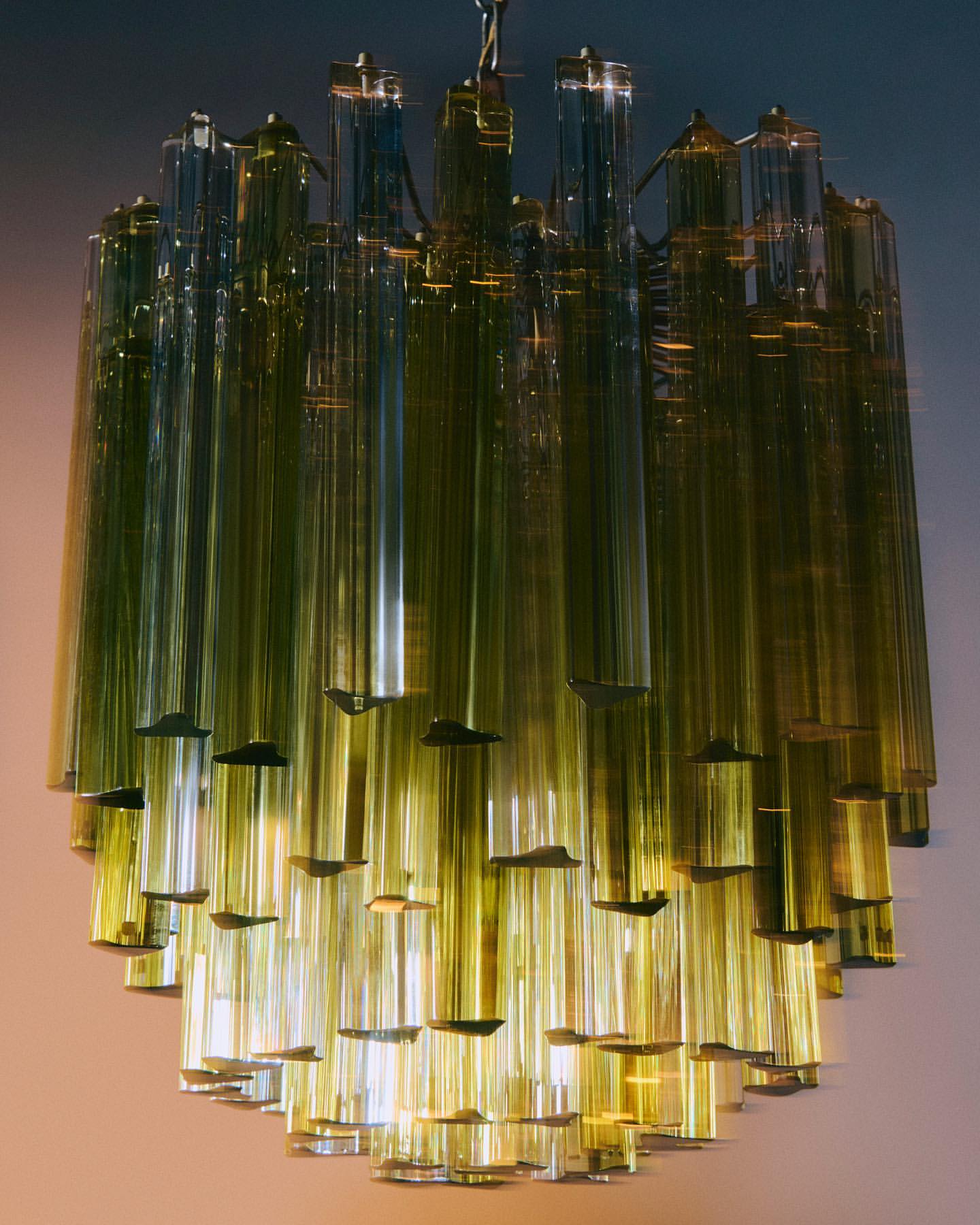 Elegant chandelier featuring numerous vertically hanging translucent tubes and decorative caps in a warm indoor setting.