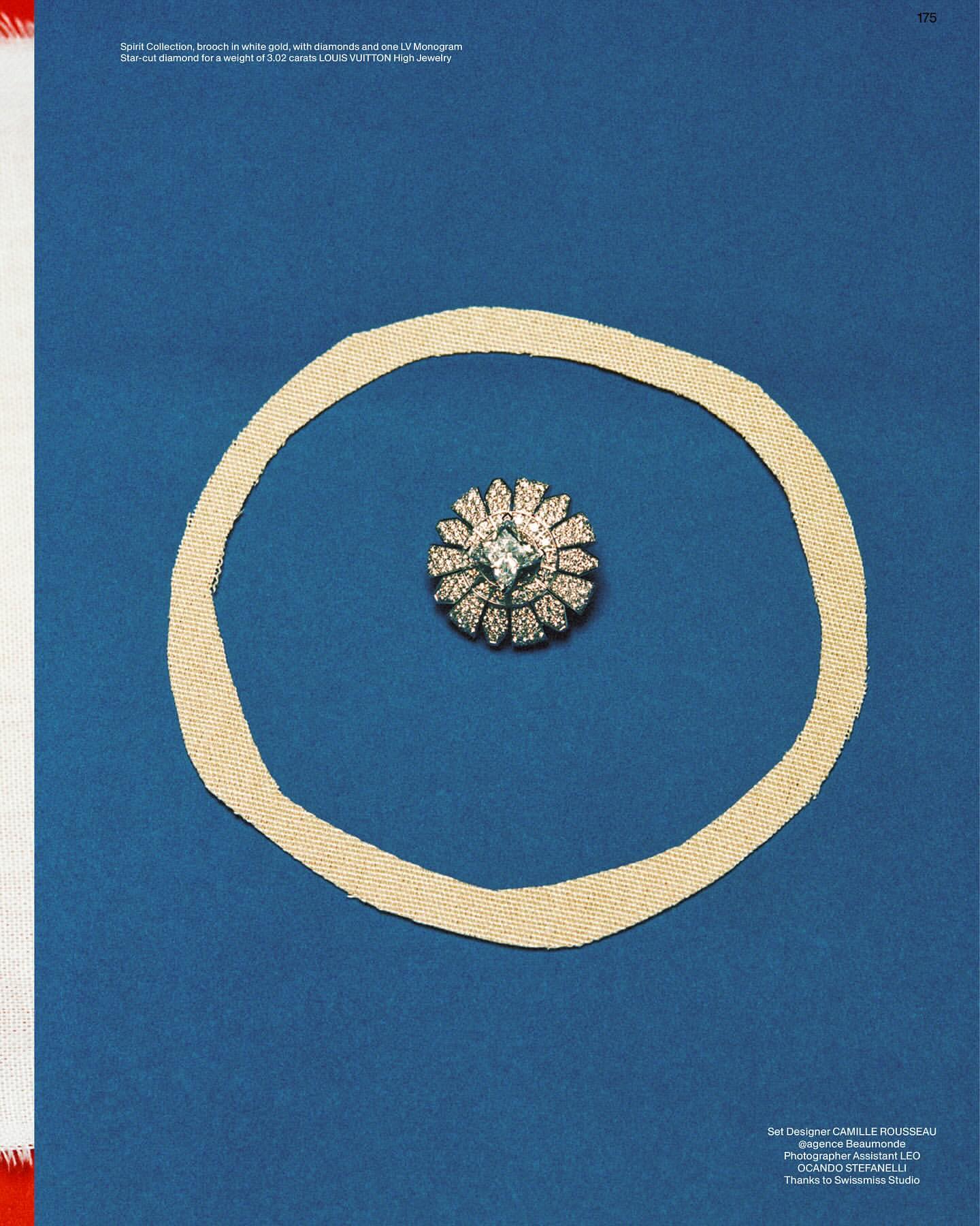 Close-up of a diamond brooch encircled by a textured ring on a blue background, evoking luxury jewelry and studio still life.