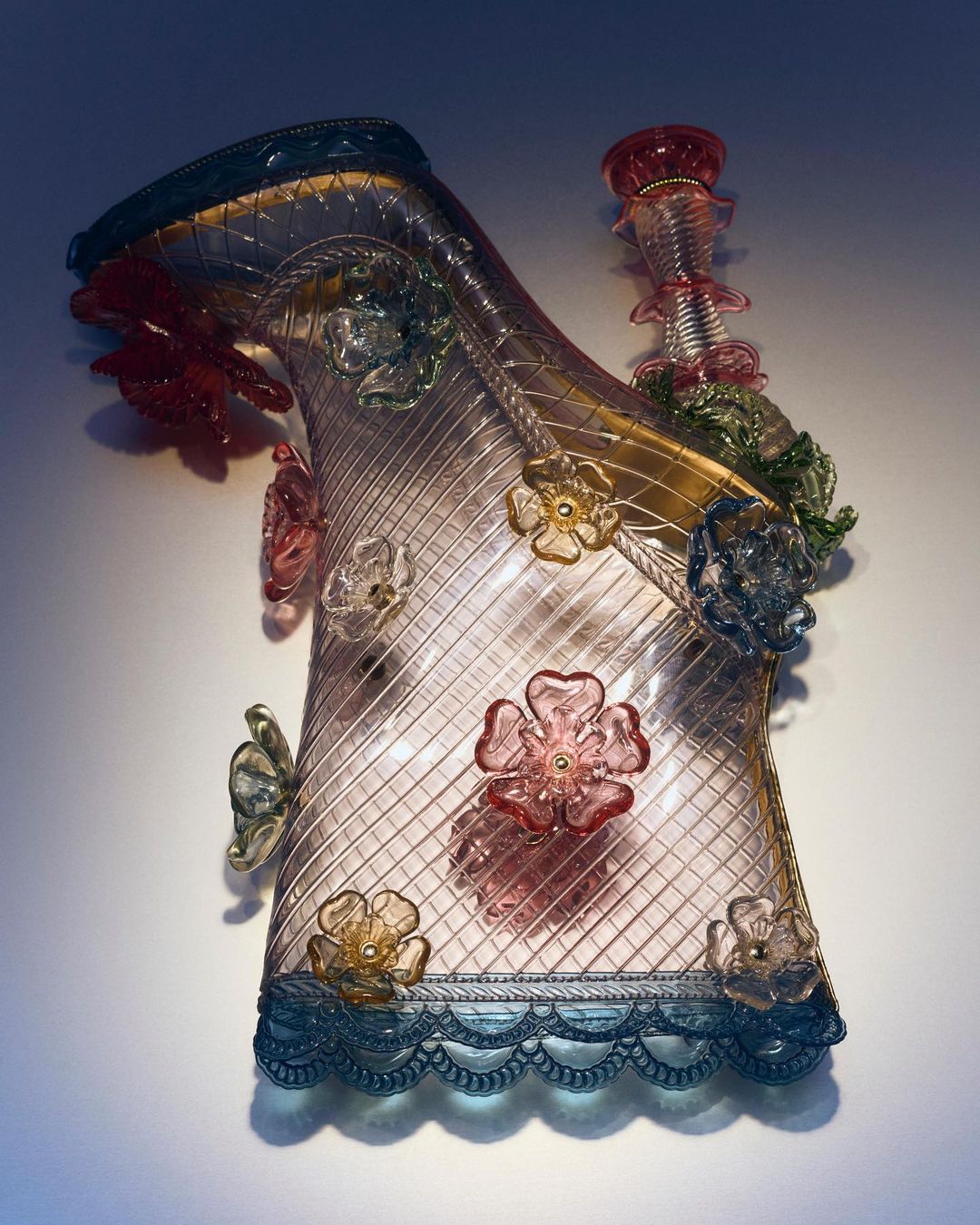 Detailed high heel glass sculpture with flower accents, lit to emphasize transparency and detail, against a simple, soft background.