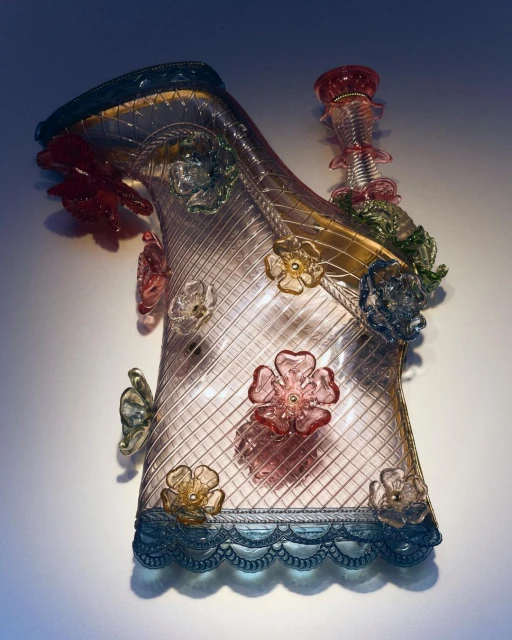 Detailed high heel glass sculpture with flower accents, lit to emphasize transparency and detail, against a simple, soft background.