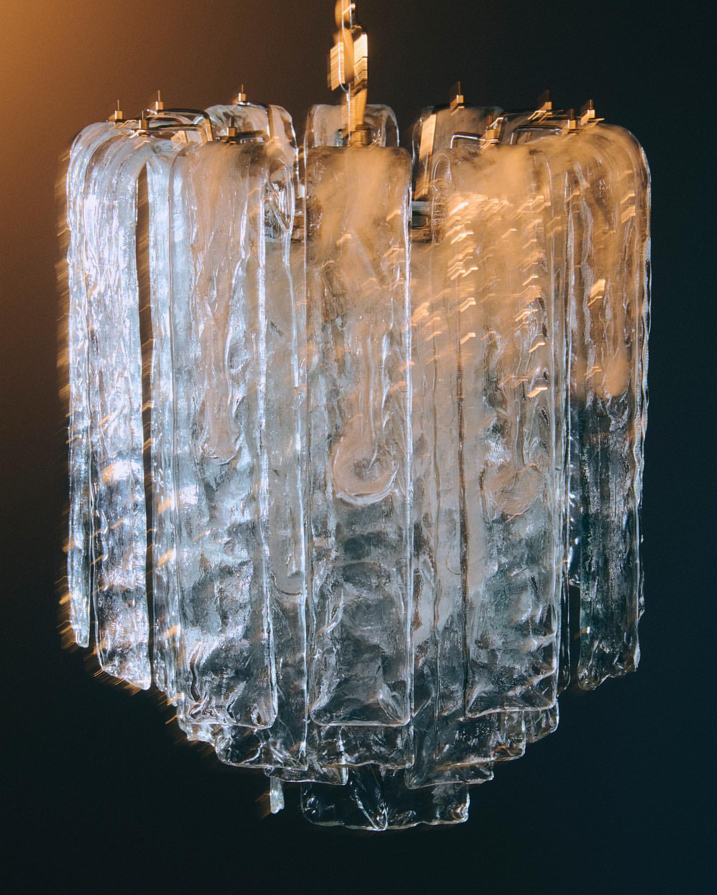 Elegant glass chandelier with tiered design and gold accents, suspended against a dark background, creating a sophisticated atmosphere.