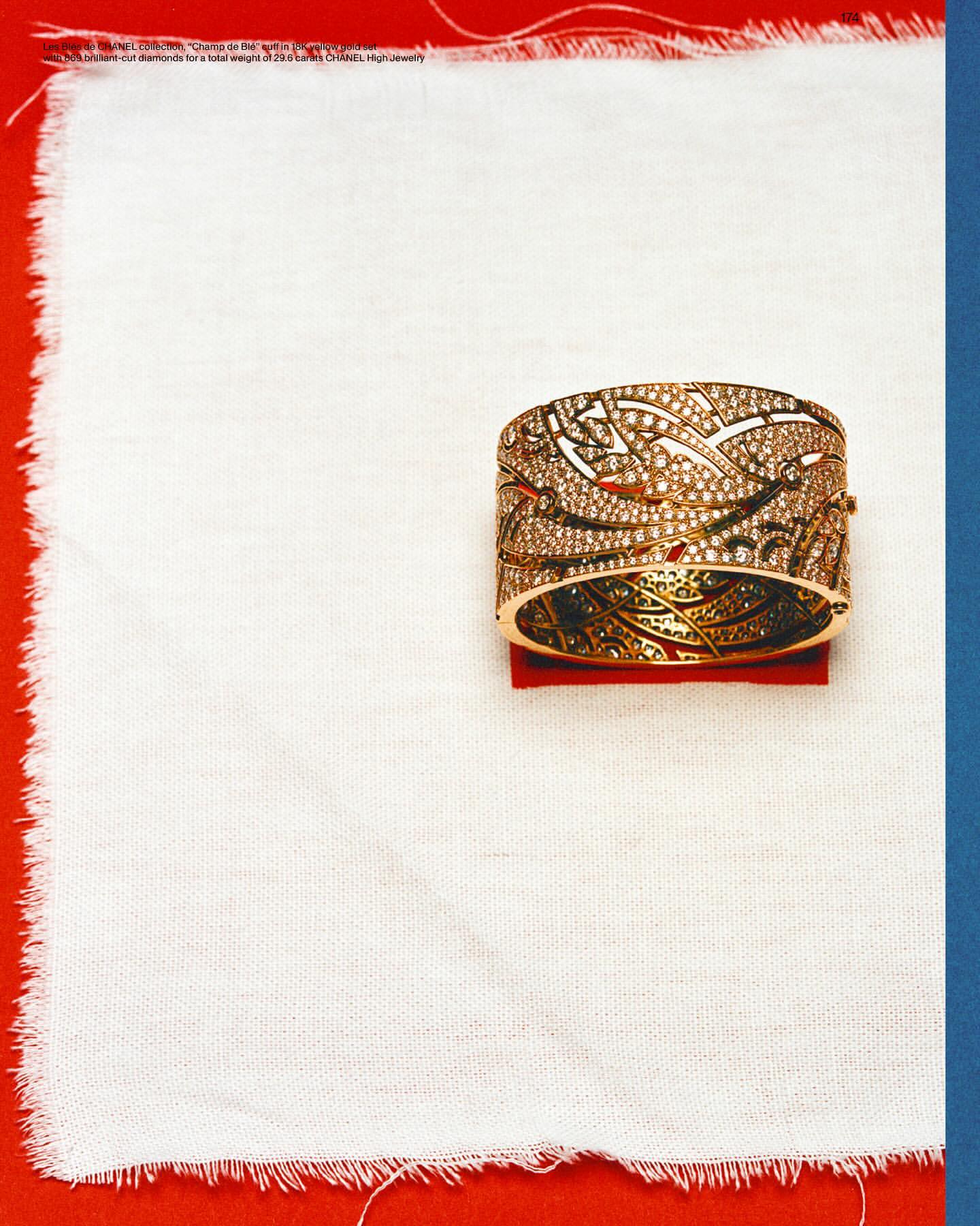 Ornate gold cuff bracelet with delicate filigree on display atop a textured white cloth against a red and blue background.