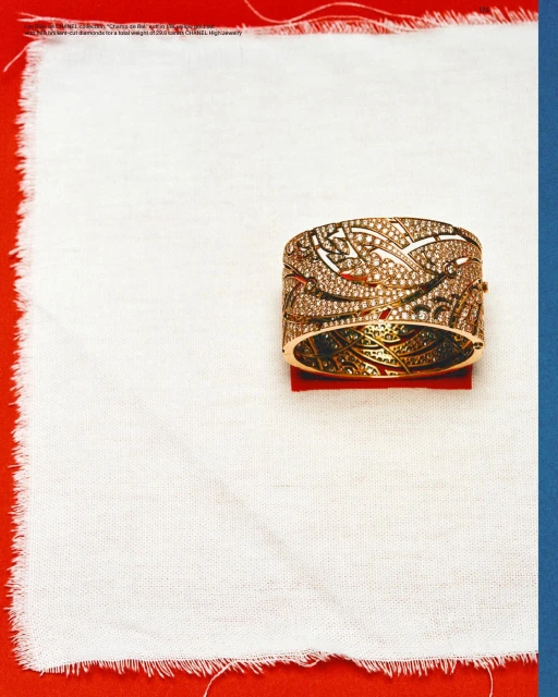 Ornate gold cuff bracelet with delicate filigree on display atop a textured white cloth against a red and blue background.