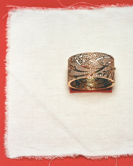Close-up of an ornate rose gold and diamond bangle bracelet on a white linen cloth atop a red background, showcasing its intricate design.