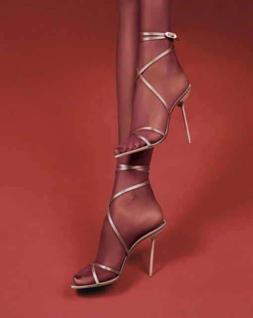 Woman's legs and feet wearing beige strappy high heels with hosiery against a red background in a studio fashion shot. 